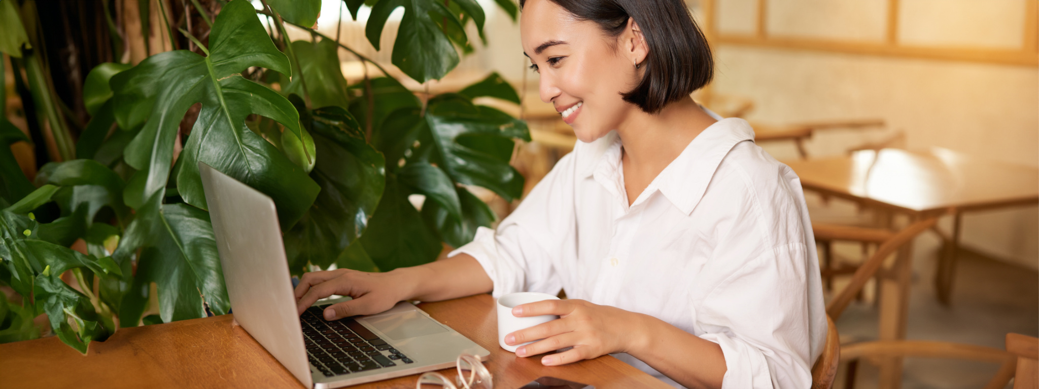 Student sitting in cafe with cup of coffee. Young asian woman working on laptop in restaurant, sitting with computer and smartphone.